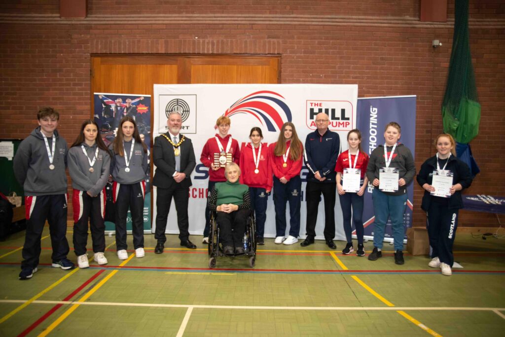 A group of medallists stand with officials and paralympic shooters.