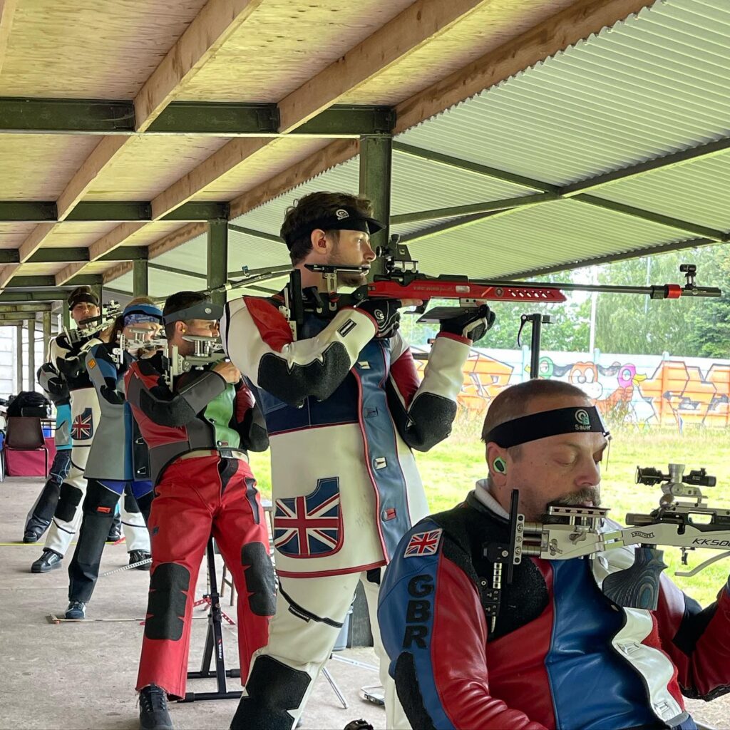 A group of paralympic and able-bodied athletes on the firing point competing in a rifle final.