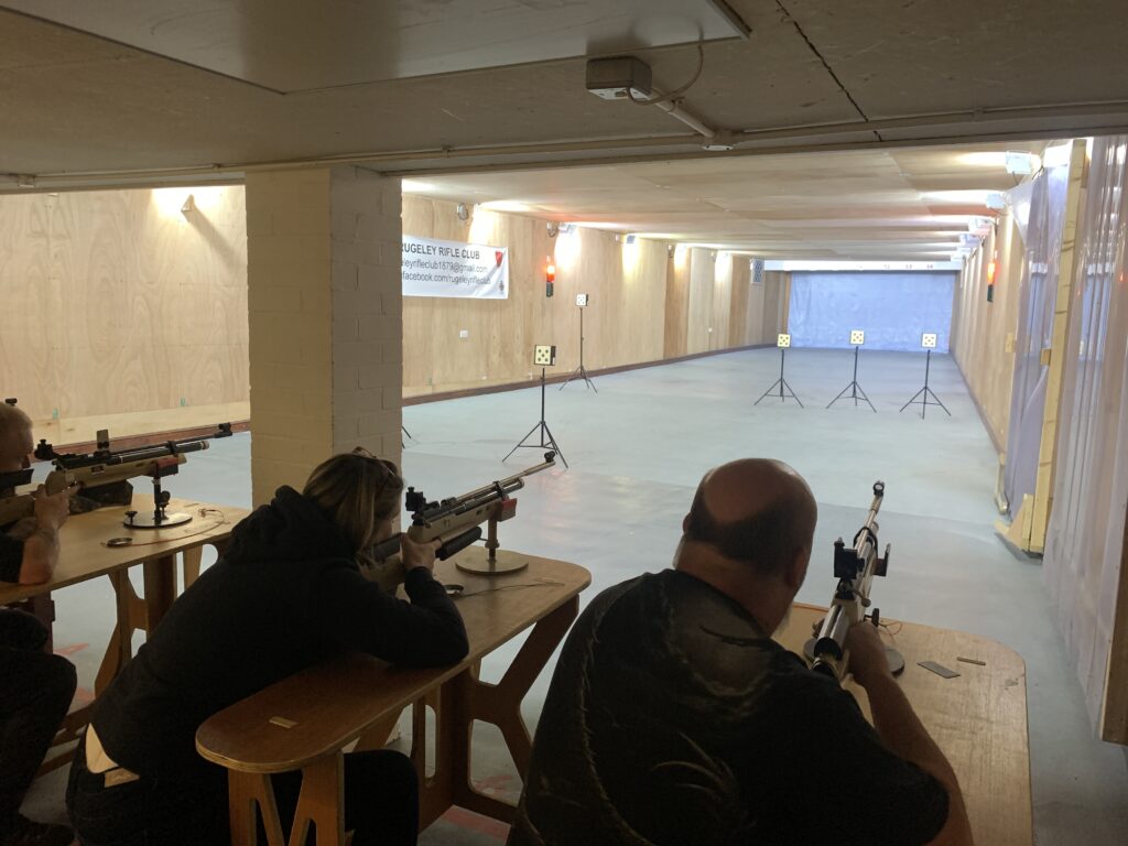 Visitors sit at benches shooting air rifles from rests. They are shooting at 10metres on the club's 25yard indoor range.