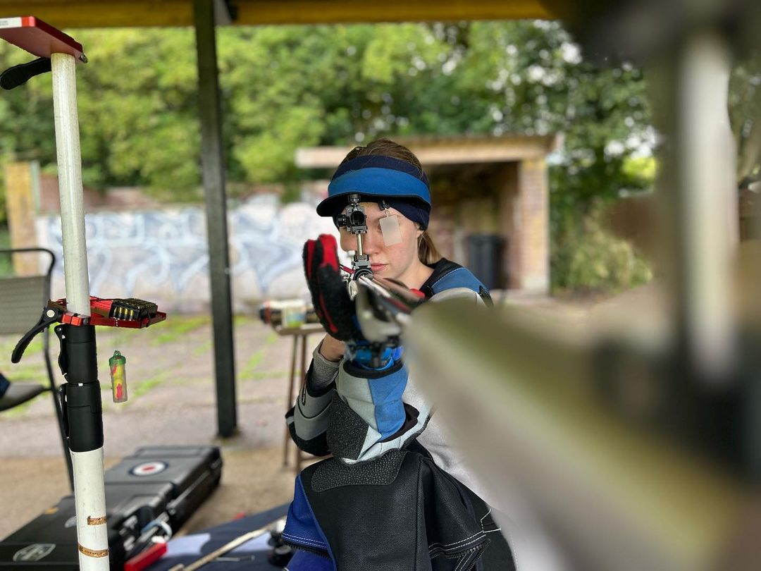 A young woman aims a precision target rifle from the kneeling position