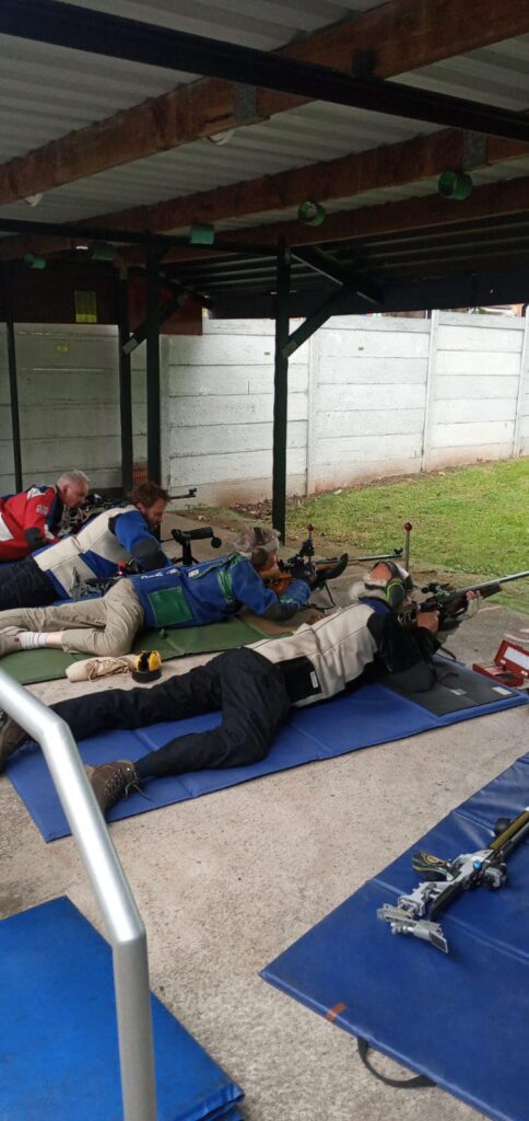 A group of target shooters on an outdoor range. The firing point is covered by a tin roof.