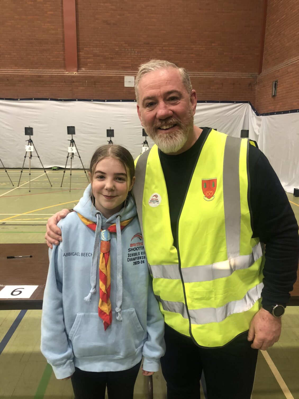A young female target shooter with a range officer. She wears a neckerchief from the Scout Association.