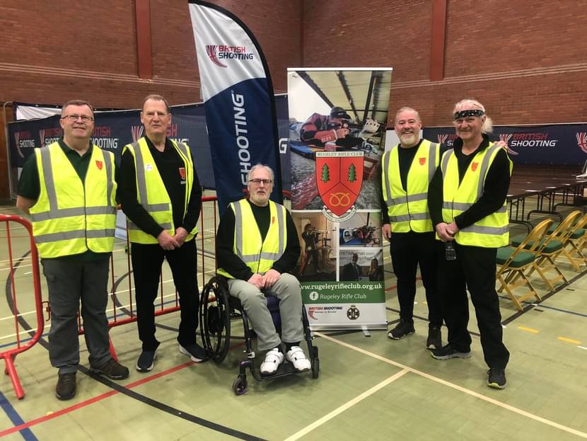 A group of adults stand in hi-vis jackets at the British Shooting Schools Rifle & Pistol Championships. They are volunteers from a local shooting club helping to run the event.