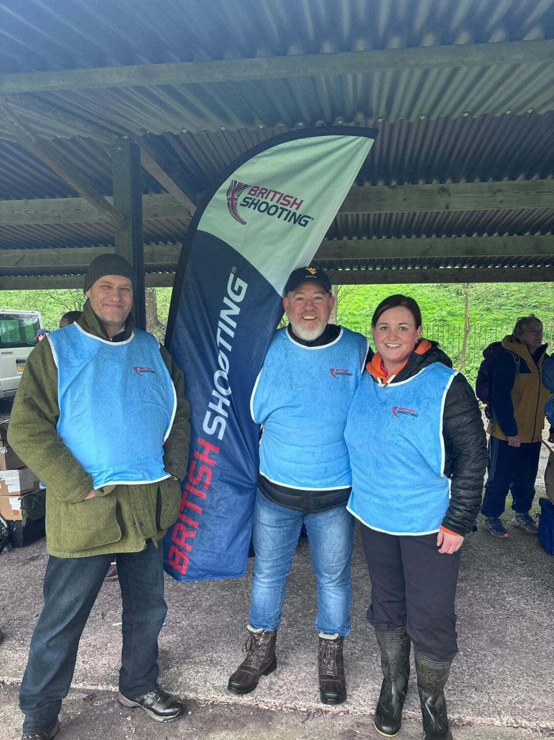 Three people stand on an outdoor range wearing blue steward tabards.