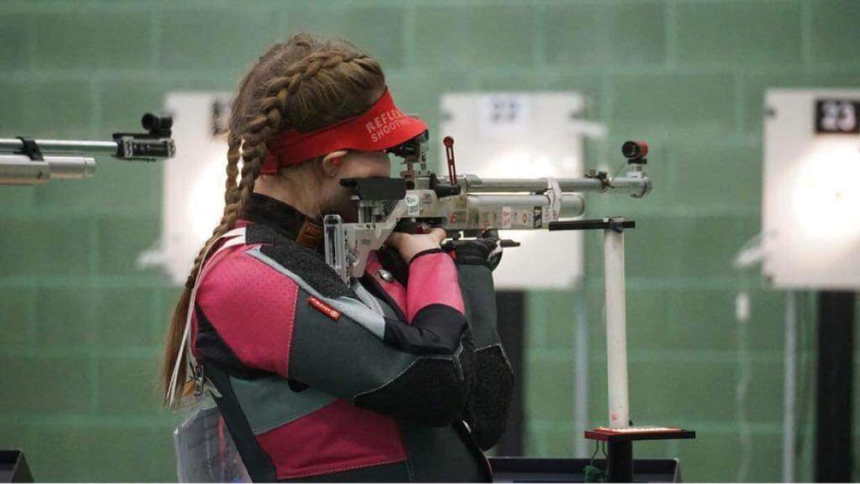 A young woman aims an air rifle in competition.