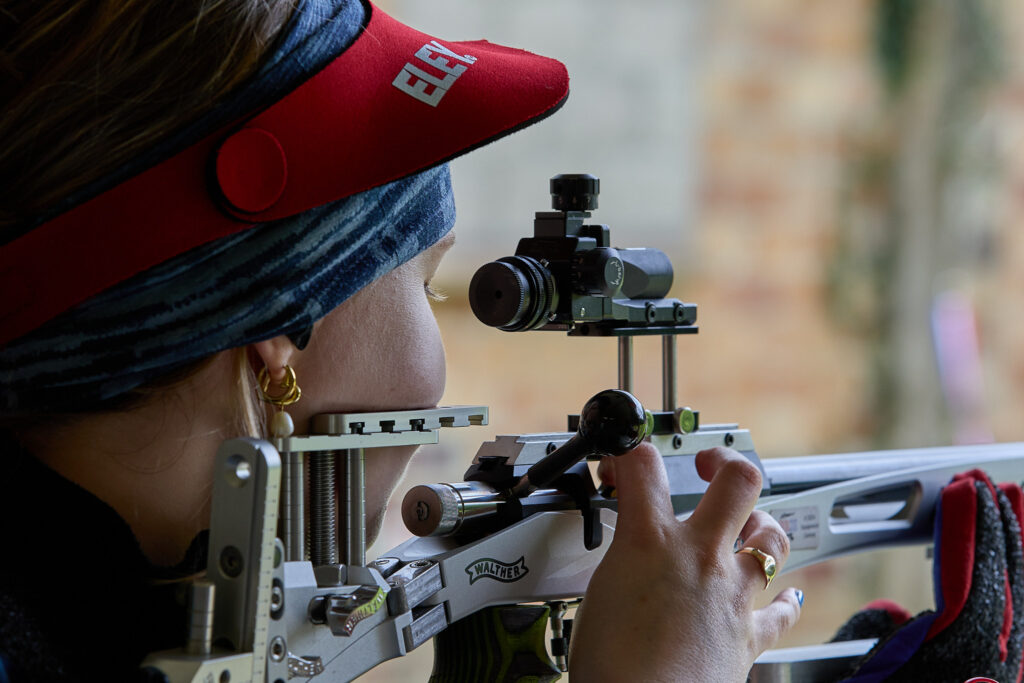 A female athlete loads a round into a smallbore target rifle The rearsight is mounted on tall sight raising blocks. The silver chassis bears the Walther logo.