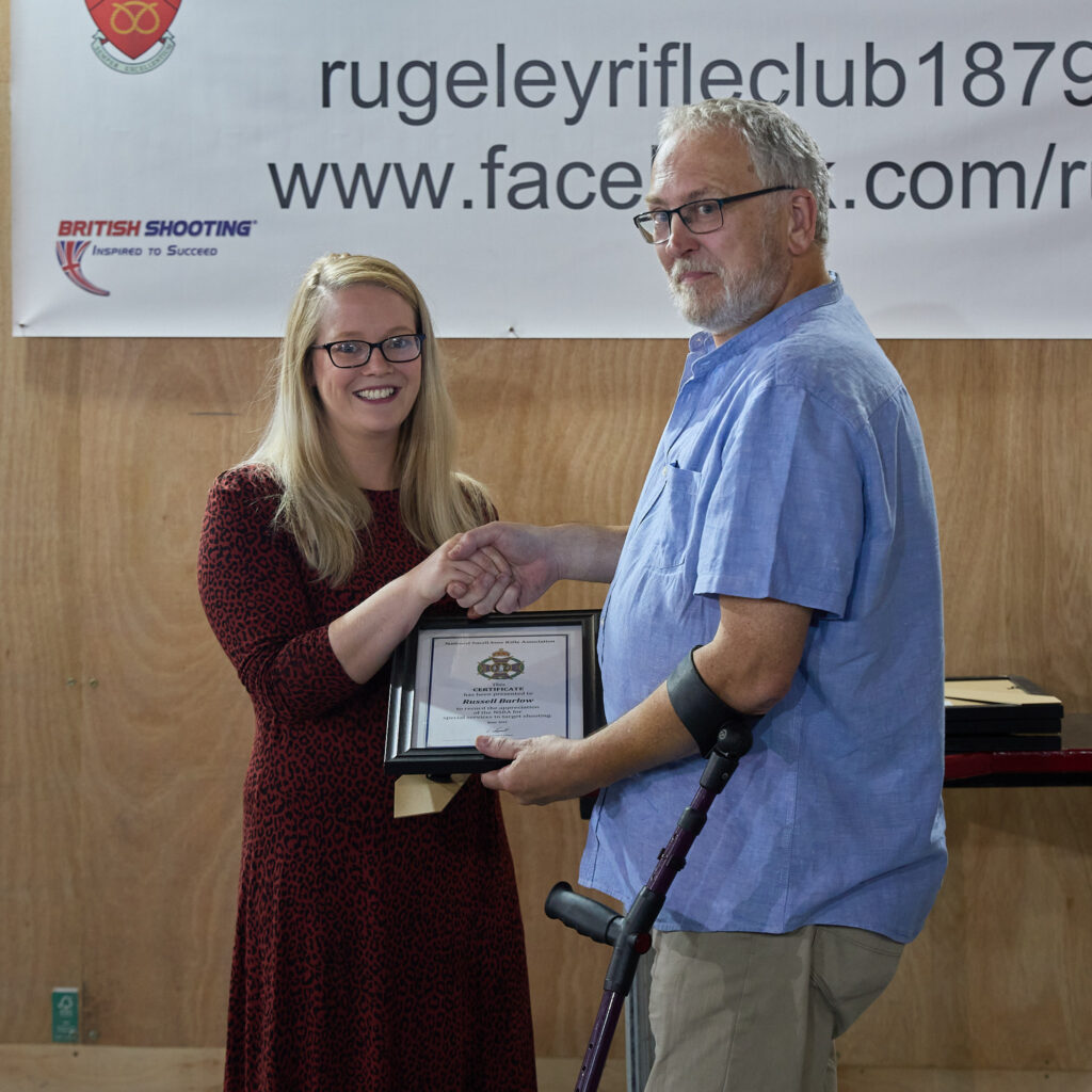 Two people smile at the camera. The woman on the left is presenting a Special Service Award to the volunteer on the right.