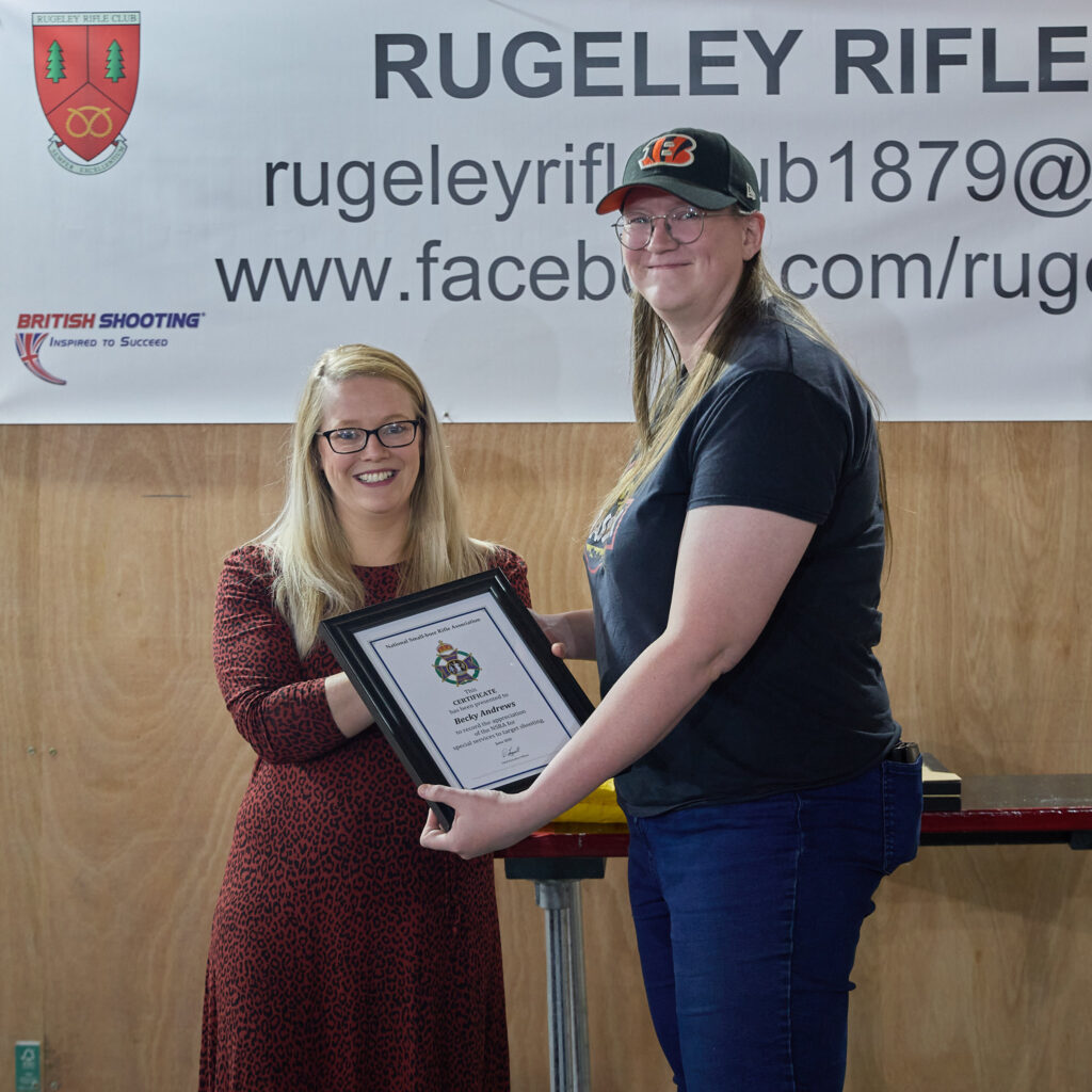 Two people smile at the camera. The woman on the left is presenting a Special Service Award to the volunteer on the right.