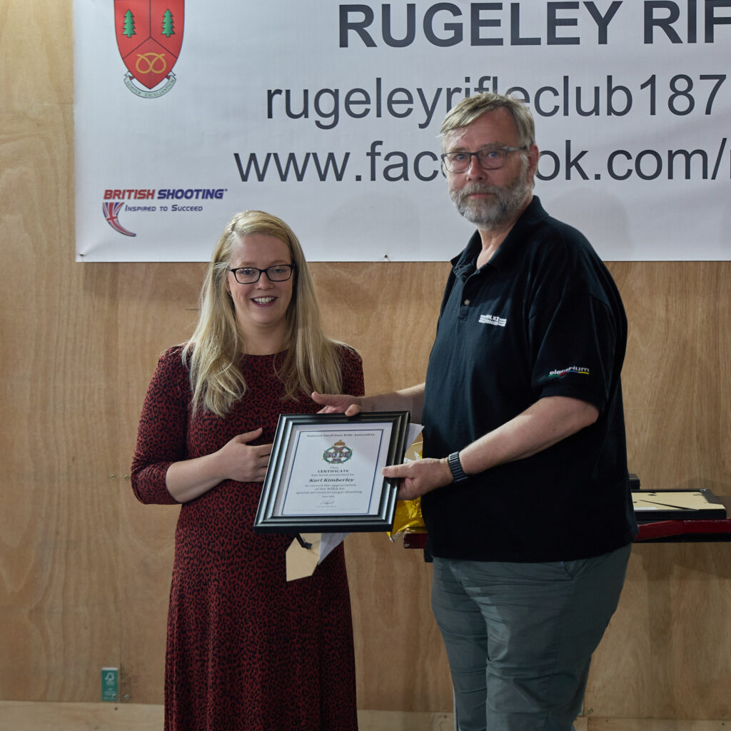 Two people smile at the camera. The woman on the left is presenting a Special Service Award to the volunteer on the right.
