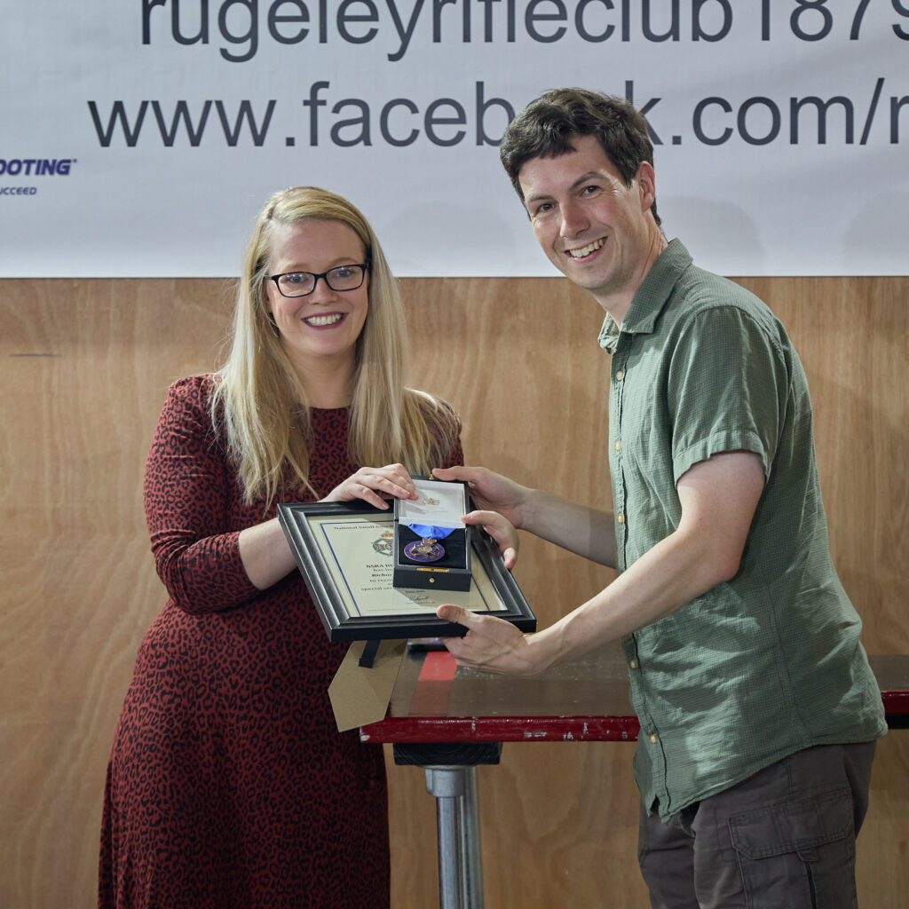 Two people smile at the camera. The woman on the left is presenting a Special Service Award to the volunteer on the right.