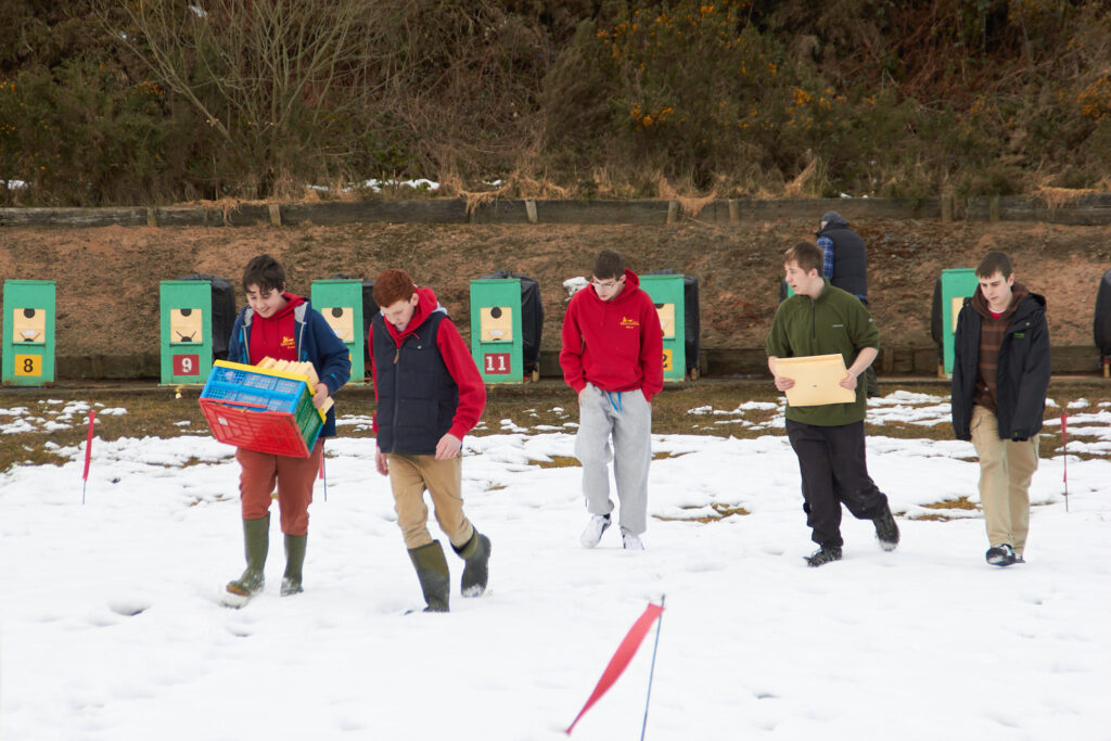 A group of young people carry stacks of targets up the snowy range.