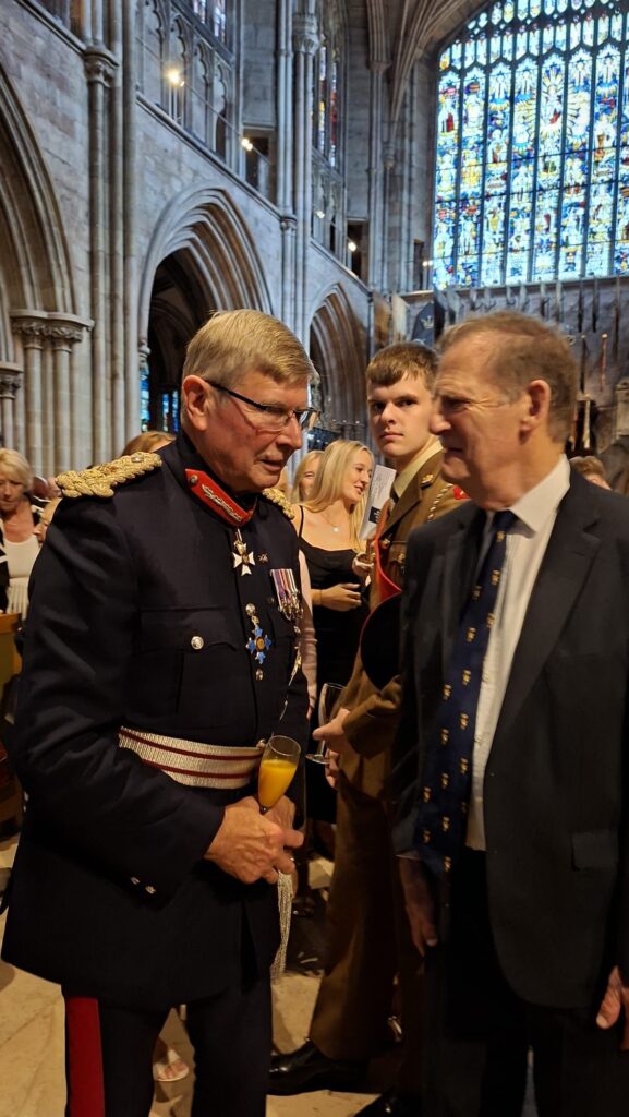 Two men stand in a cathedral. The one on the left wears the uniform of the Lord Lieutenant. The other is suited.