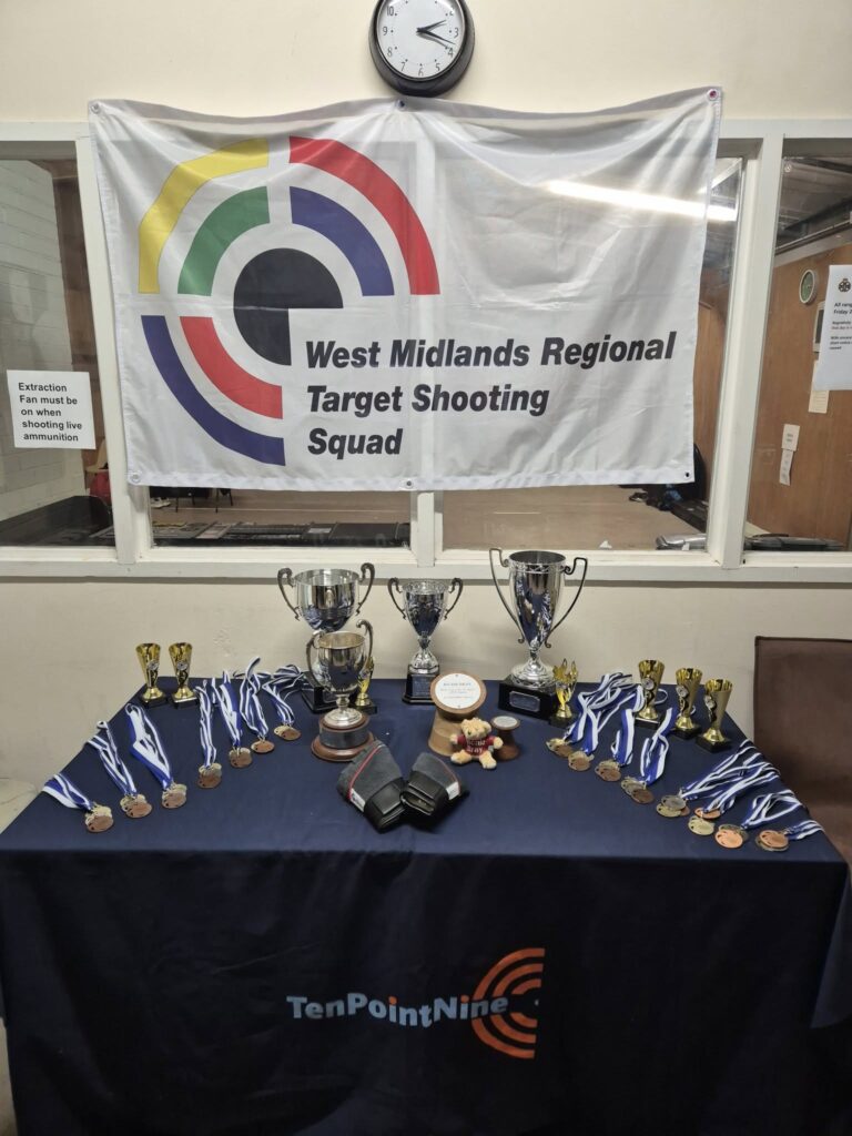 A table laden with trophies and medals. A flag behind reads "West MIdlands Regional Target Shooting Squad".